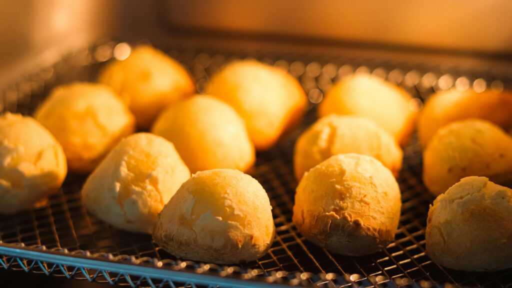 Freshly baked cheese bread rolls on a rack with warm lighting in the oven.